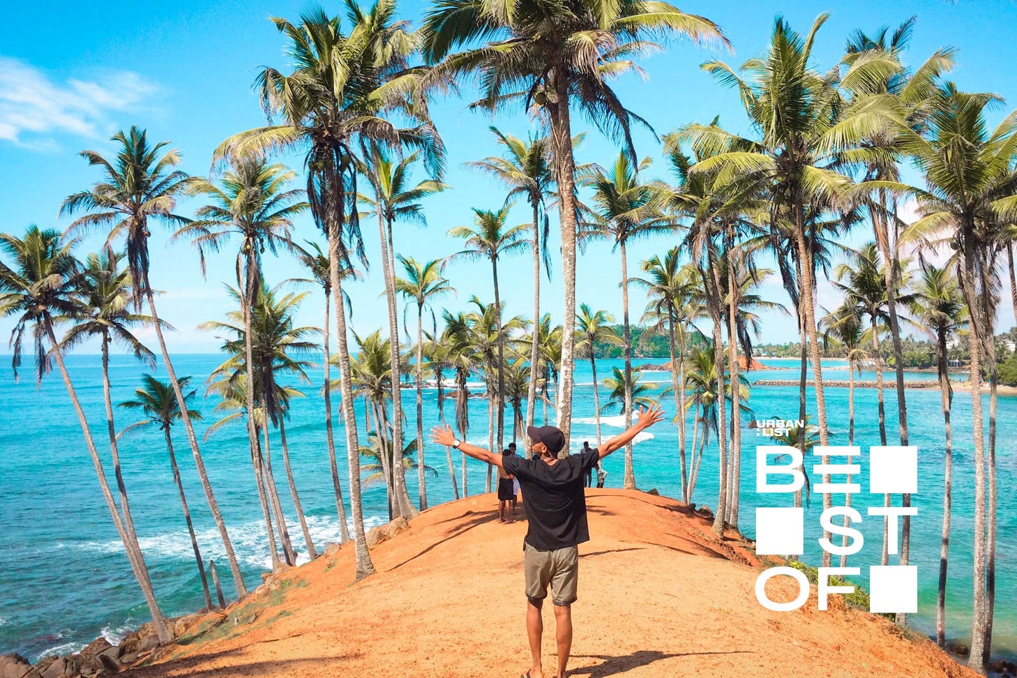 a person standing on the edge of a sandy cliff with palm trees with their hands in the air